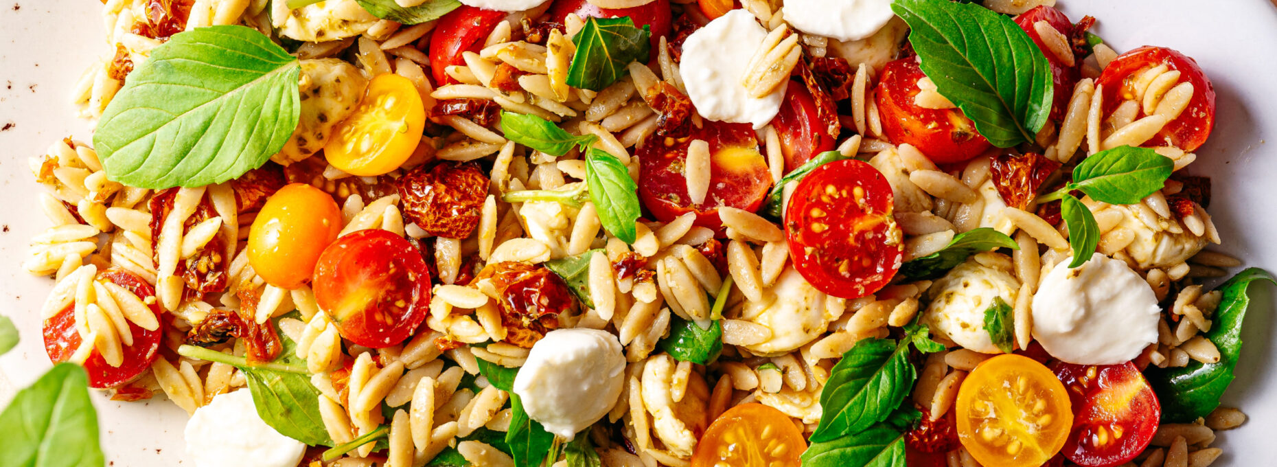 Een foto van een recept voor een zomerse orzo salade, met pesto, mozzarella en basilicum, in een witte schaal