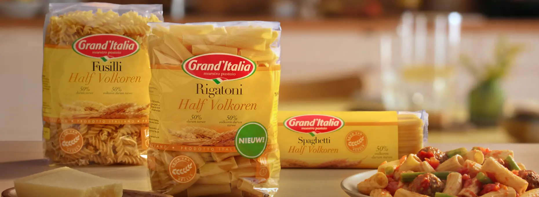 Afbeelding van een aanrecht met daarop een bord pasta rigatoni. Op het aanrecht staan ook de verpakkingen van de Half Volkoren pasta's, namelijk Fusilli Half Volkoren, Spaghetti Half Volkoren en in het midden de nieuwe Rigatoni Half Volkoren.