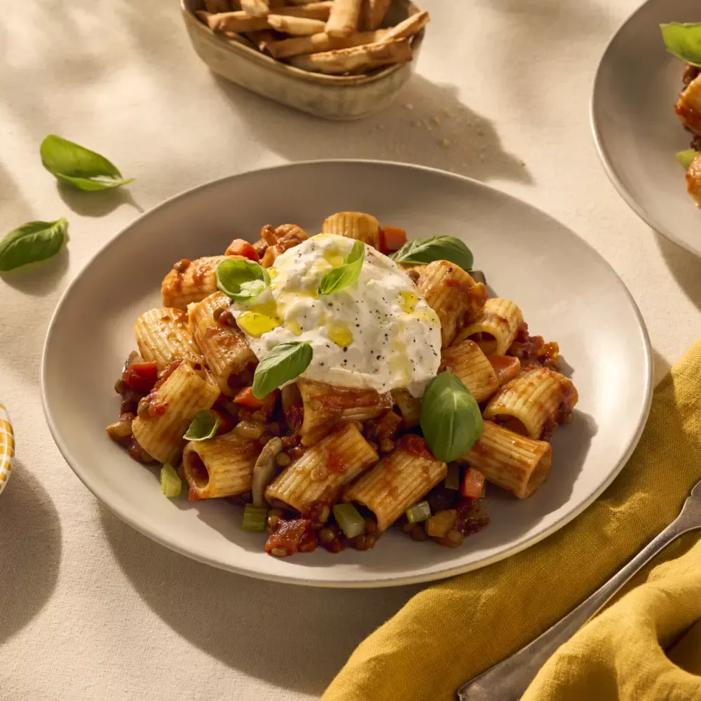 Een heerlijk bordje pasta met halve rigatoni. De geribbelde buisjespasta houdt de vegetarische bolognesesaus (gemaakt van linzen) goed vast en dat zie je goed op de afbeelding. Het gerecht is gegarneerd met wat verse basilicum blaadjes en bovenop ligt een heerlijke burrata.