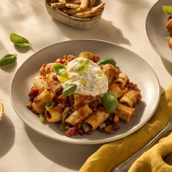 Een heerlijk bordje pasta met halve rigatoni. De geribbelde buisjespasta houdt de vegetarische bolognesesaus (gemaakt van linzen) goed vast en dat zie je goed op de afbeelding. Het gerecht is gegarneerd met wat verse basilicum blaadjes en bovenop ligt een heerlijke burrata.