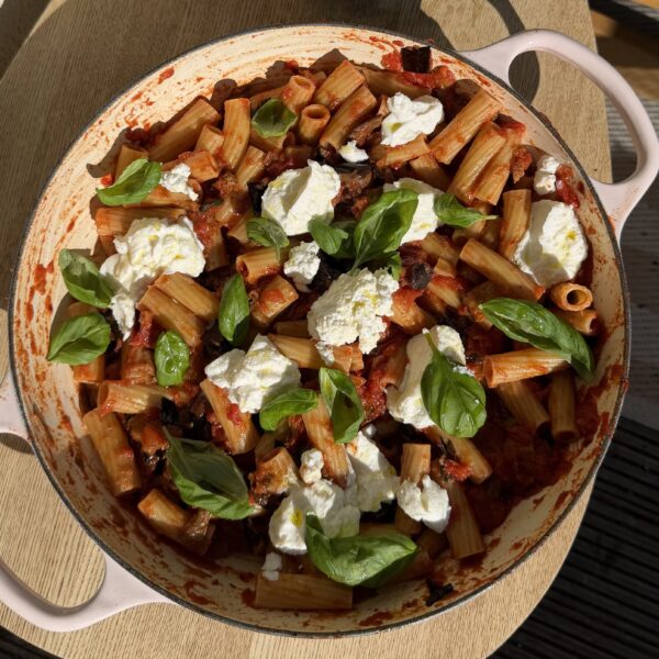 Foto van de rigatoni alla norma in een pan. De Sugocasa is gemengd met de Rigatoni Half Volkoren en bovenop liggen schepjes ricotta en verse basilicumblaadjes als garnering en voor extra smaak.