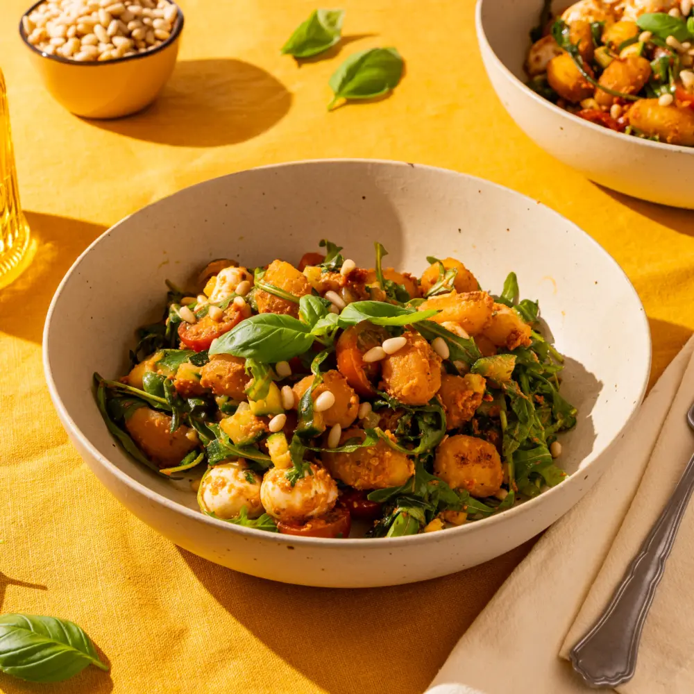 Een heerlijk bordje met crispy gnocchi en rode pesto. In het gerecht is de rode pesto goed te zien, samen met de courgette, cherrytomaatjes en mozzarella. Rucola, pijnboompitten en een plukje verse basilicum maken het af.