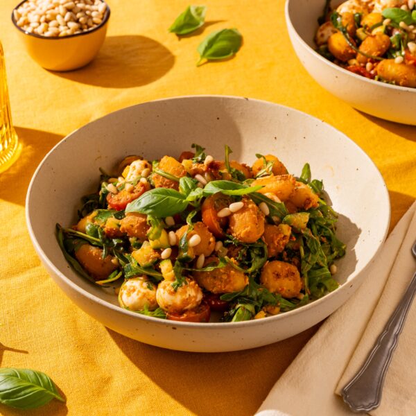Een heerlijk bordje met crispy gnocchi en rode pesto. In het gerecht is de rode pesto goed te zien, samen met de courgette, cherrytomaatjes en mozzarella. Rucola, pijnboompitten en een plukje verse basilicum maken het af.