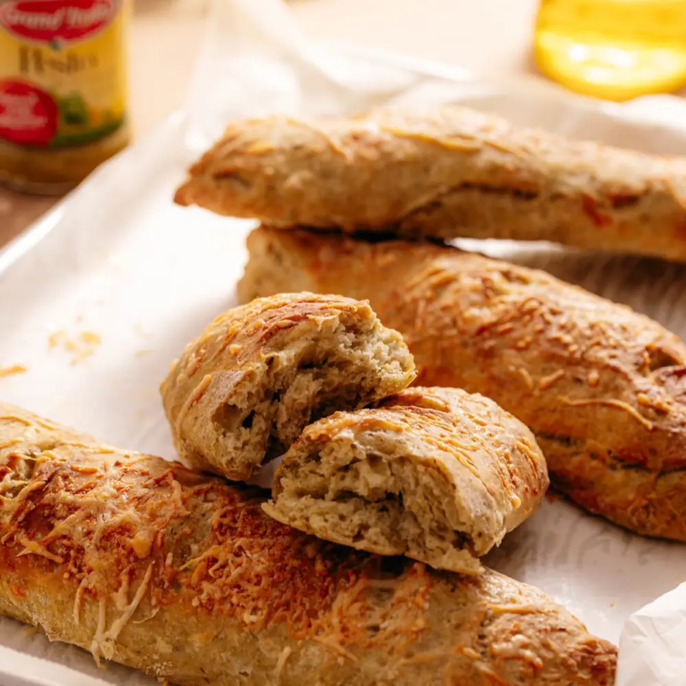 Heerlijke pistolet/baguette vormige broodjes. Eén van de broodjes is opengesneden en in het midden zie je hoe luchtig de broodjes zijn en kun je de pesto zien. Op de achtergrond is ook nog een potje Pesto alla Genovese van Grand'Italia zichtbaar.