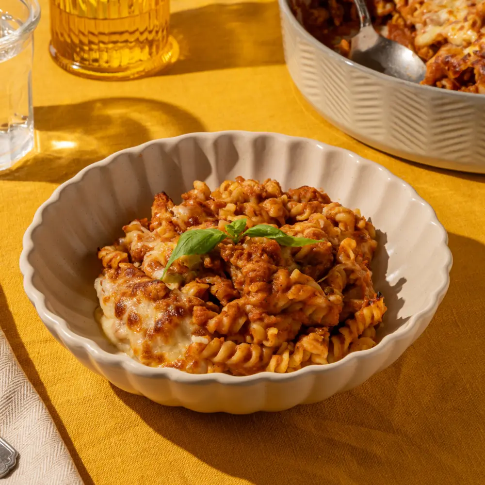 Een heerlijk vrolijk bordje pasta. Het bordje heeft een mooie schelprand en de pasta komt er goed in uit. Je ziet dat de gepureerde saus (van alle groenten) goed in de ribbels van de fusilli blijft zitten. Bovenop ligt als garnering een takje verse basilicum.