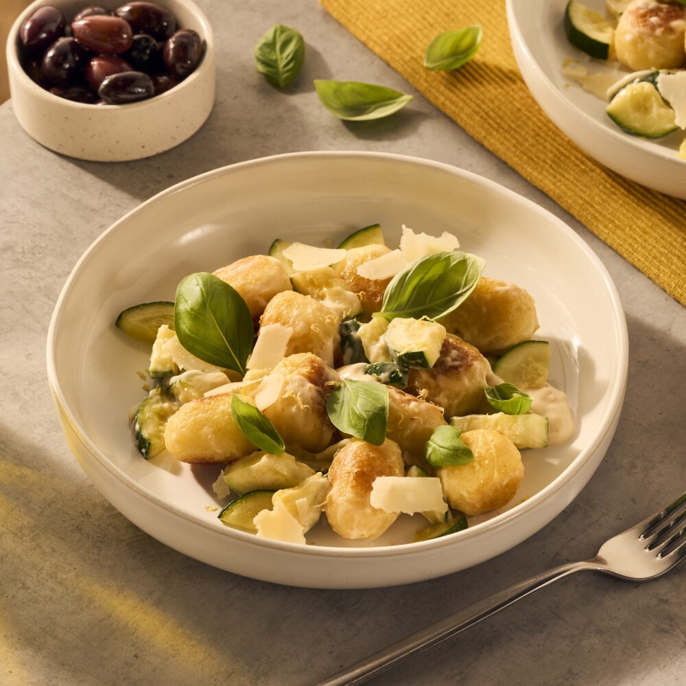 Een heerlijk bordje met gevulde gnocchi. De gnocchi ballen worden rijk omhuld door de romige Romana pastasaus en het gerecht is gegarneerd met basilicumblaadjes en Parmezaanse kaas flakes. Er schijnt een lekker zonnetje op het bord.