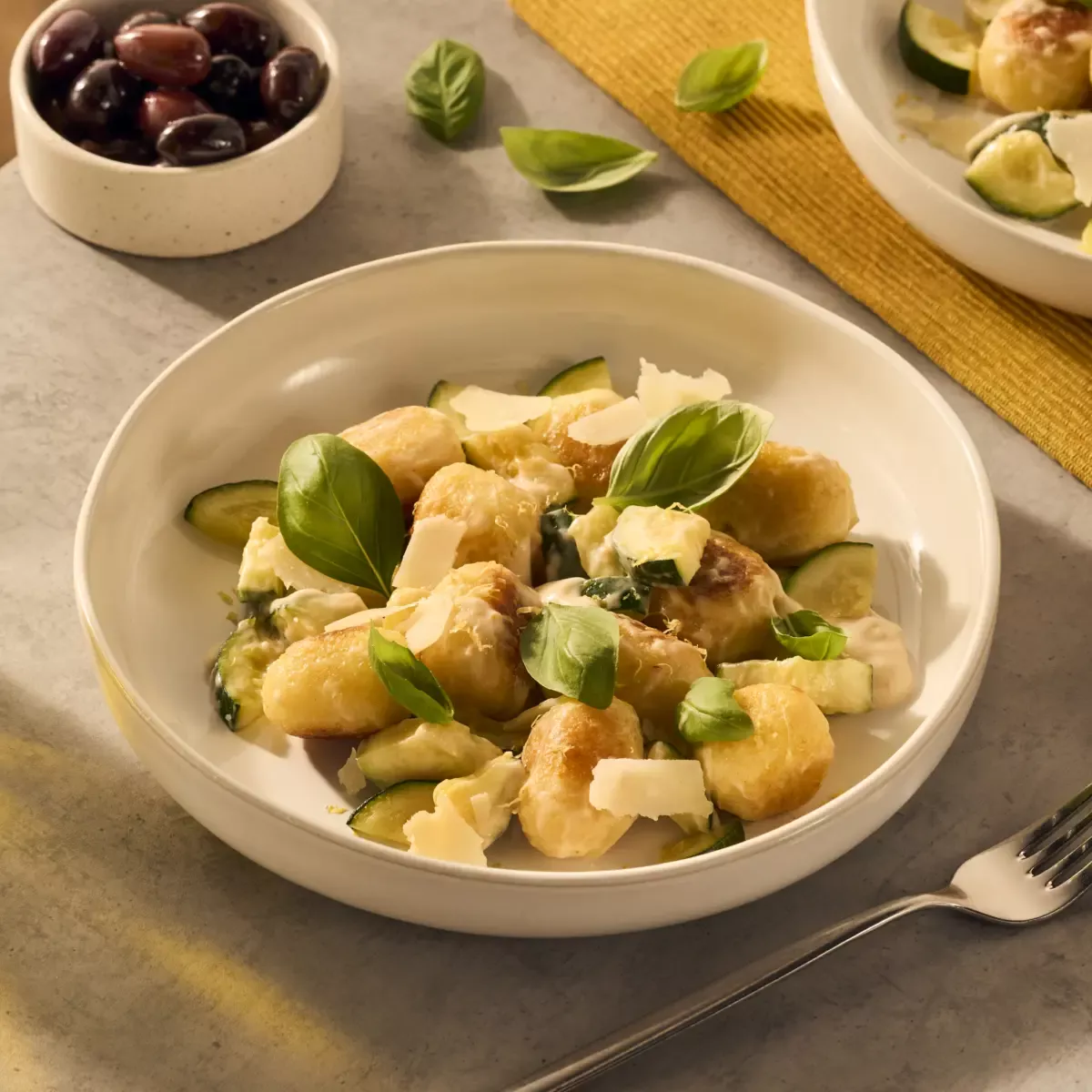 Een heerlijk bordje met gevulde gnocchi. De gnocchi ballen worden rijk omhuld door de romige Romana pastasaus en het gerecht is gegarneerd met basilicumblaadjes en Parmezaanse kaas flakes. Er schijnt een lekker zonnetje op het bord.