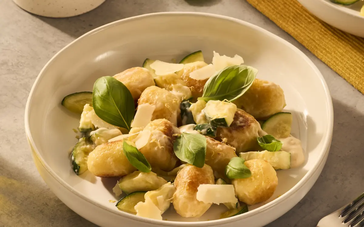 Een heerlijk bordje met gevulde gnocchi. De gnocchi ballen worden rijk omhuld door de romige Romana pastasaus en het gerecht is gegarneerd met basilicumblaadjes en Parmezaanse kaas flakes. Er schijnt een lekker zonnetje op het bord.