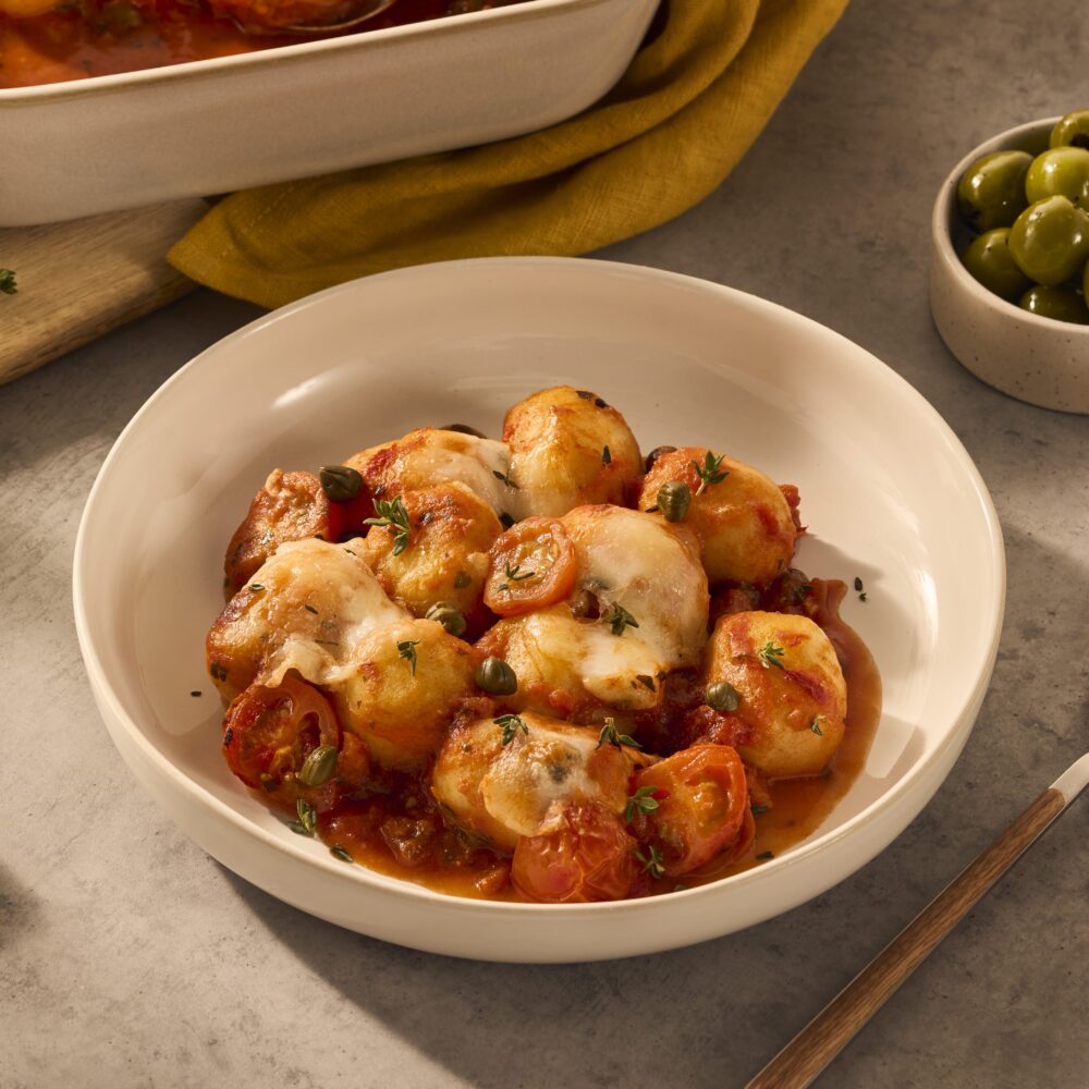 Een heerlijk gerecht in een wit diep bord, met gevulde gnocchi, dieprode tomatensaus en heerlijke mozzarella die over de gnocchi heen gesmolten is.