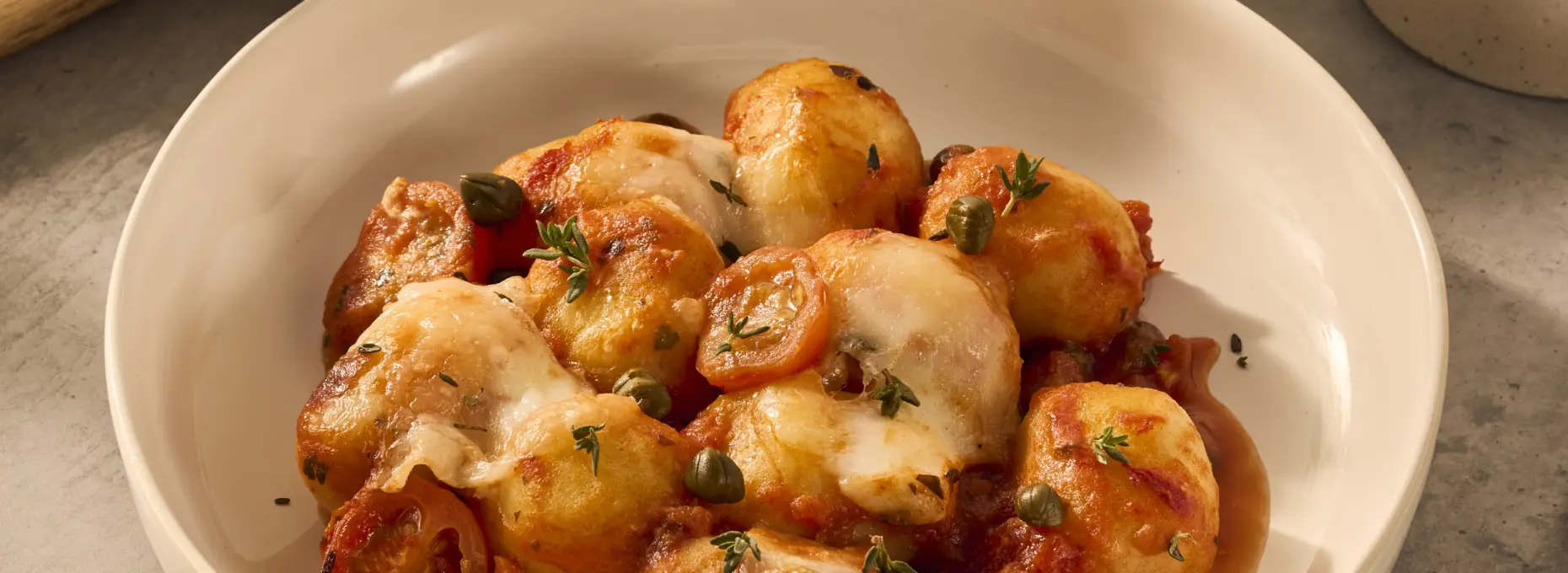 Een heerlijk gerecht in een wit diep bord, met gevulde gnocchi, dieprode tomatensaus en heerlijke mozzarella die over de gnocchi heen gesmolten is.