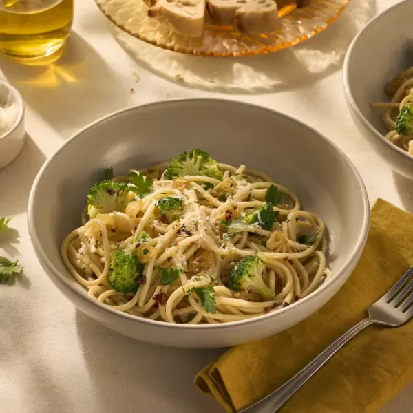 Op de afbeelding zie je een bord pasta met chitarra (een soort vierkante spaghetti), omhult met olijfolie, chilivlokken en knoflook. Tussen de pasta zitten groene verse roosjes broccoli en het gerecht is getopt met geraspte Parmezaanse kaas.